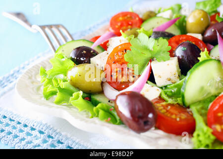 Delicious fresh mixed Greek salad with crispy lettuce, cherry tomato, onion, cucumber, olives and feta cheese served on a white Stock Photo