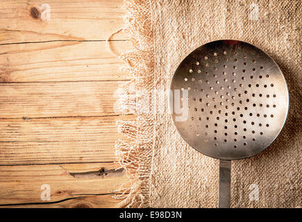 Old circular metal colander, sieve or strainer with perforated holes for draining vegetables while preparing a meal in a country kitchen over a textured wooden background with copyspace Stock Photo