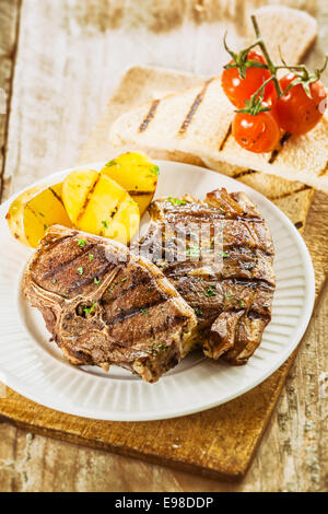 Delicious barbecued lunch on a summer picnic with grilled lamb chops, potatoes, tomatoes and slices of toast for a nutritious meal Stock Photo