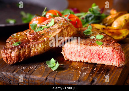 Delicious portion of healthy grilled lean medium rare beef steak cut through and served on a wooden kitchen board garnished with fresh herbs Stock Photo