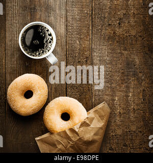 Close up overhead view of two delicious sugared ring doughnut with espresso coffee and crumpled brown paper packet on a rustic wooden surface with copyspace for a relaxing coffee break Stock Photo