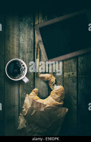 Overhead view of a vintage blank school slate with a cup of strong black espresso coffee and a crescent shaped crispy croissant Stock Photo
