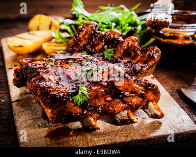 Delicious barbecued ribs seasoned with a spicy basting sauce and served with chopped fresh herbs on an old rustic wooden chopping board in a country kitchen Stock Photo