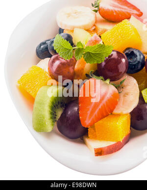 Healthy dessert of fresh tropical fruit salad with colorful berries, kiwifruit, banana, grapes, apples and orange garnished with peppermint leaves in a close up overhead view Stock Photo