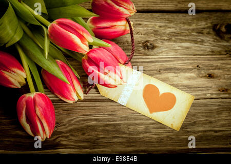 Bouquet of red tulips with a vintage red heart gift tag lying on rustic weathered wooden boards, closeup overhead view with copyspace for a loving message on Valentines Day or an anniversary Stock Photo