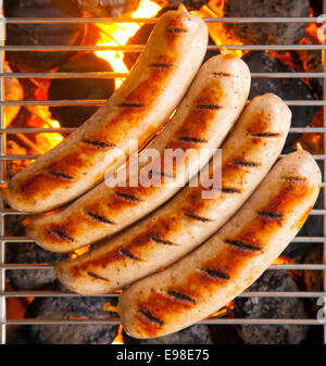 Delicious sausages called bratwurst, on a metal grid grilling over hot coals on a BBQ for a picnic lunch on a summer vacation Stock Photo