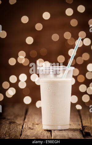 Rich creamy smoothie or milkshake blend on a party background of sparkling defocused lights standing on a rustic wooden table Stock Photo