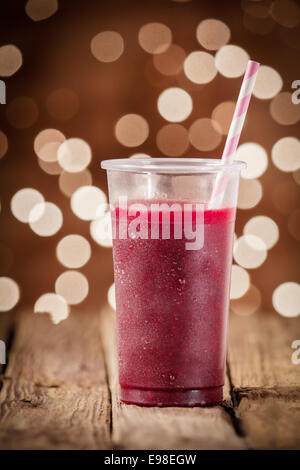 Glass of healthy blueberry smoothie served on an old rustic wooden taable against a festive background bokeh of twinkling parfty lights