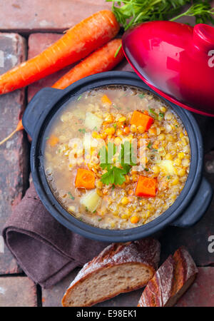 Overhead view of a thick wholesome vegetarian vegetable and lentil stew served with sliced bread on bricks Stock Photo