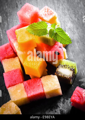 Pile of diced and cubed fresh summer fruit being prepared for a gourmet dessert with watermelon, pineapple, melon, orange, and kiwifruit on a slate kitchen counter Stock Photo