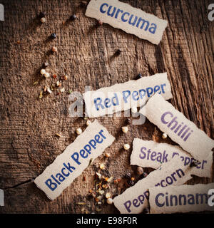 Scattered decorative name labels for spices with black and white peppercorns on a textured weathered wood surface with copyspace Stock Photo