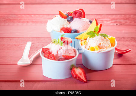 Delicious fresh tropical fruit and assorted berries served with frozen yoghurt or ice cream in three individual servings on a pink wood background with vignette Stock Photo