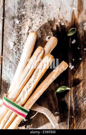 Italian grissini bread sticks made from crisp golden baked unleavened dough, tied in a bundle with a ribbon with the colors of the Italian national flag lying on a grunge rustic wooden table Stock Photo