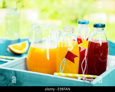 Healthy freshly squeezed fruit juice with bottles of orange citrus blend and fresh berry juice standing on a turquoise picnic table in a summer garden Stock Photo