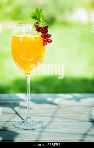 Stylish glass of orange and champagne cocktail to celebrate a special occasion garnished with delicious red currants standing on a sunny table in the garden on a summer day Stock Photo