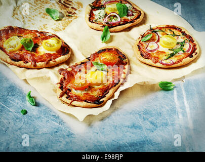 Four freshly baked Italian mini pizzas with a cheese, tomato and fresh basil topping on grungy stained oven paper with copyspace Stock Photo