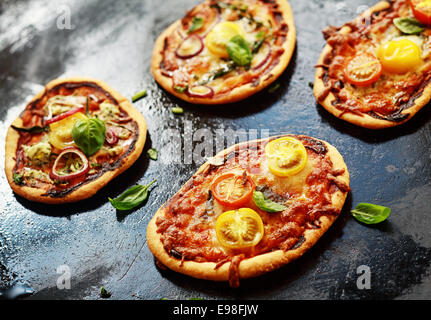 Selection of mini Italian vegetarian pizzas topped with cheese, onion, tomato and basil in a cafeteria or pizzeria for a tasty midday snack Stock Photo