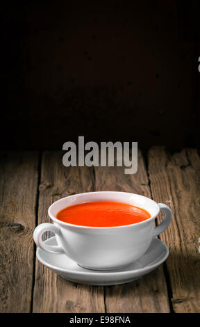 Plain white ceramic bowl of delicious hot tomato soup for a cold winter night served on rustic wooden boards with copyspace above Stock Photo