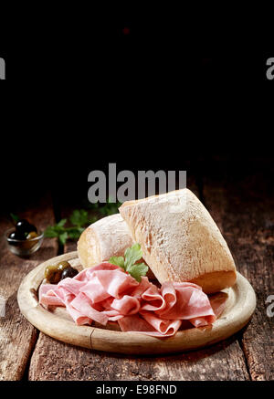 Cured thinly sliced German ham with crusty rolls for a country lunch served on a wooden platter with copyspace, vertical format Stock Photo