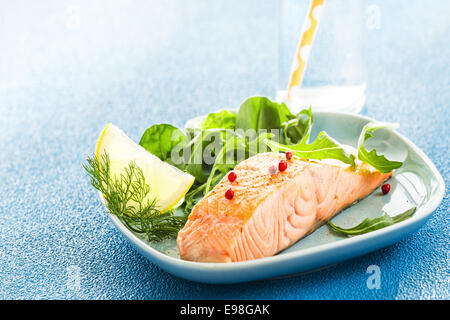 Grilled pink salmon steak served with green salad, dill and a lemon wedge for seasoning on a textured blue background with copyspace Stock Photo