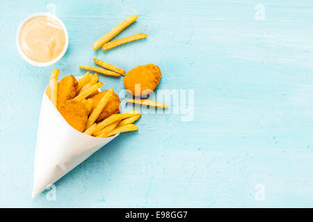 Overhead view on a blue background with copyspace of medallions of fried fish and chips in a takeaway paper cone with savory mayonnaise dip Stock Photo