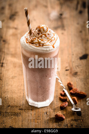 Glass of thick creamy coffee milkshake, frappe or iced coffee with a topping of ice cream and drizzled syrup on an old wooden table, high angle view Stock Photo