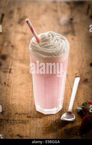 Delicious berry smoothie or milkshake served in a tall glass topped with a twirl of whipped cream or frozen yoghurt, high angle