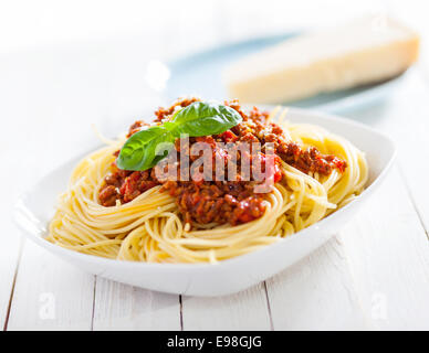 Healthy plate of Italian spaghetti topped with a tasty tomato and ground beef Bolognese sauce and fresh basil on a rustic white Stock Photo