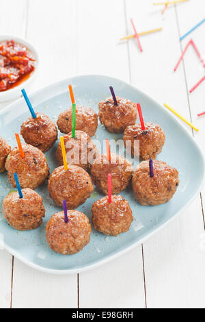 Preparing a tray of delicious spicy seasoned meatballs with colored toothpicks for snacks at a catered event , high angle view on a plate on rustic white boards Stock Photo