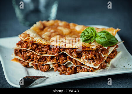 Italian beef lasagne with spicy seasoned ground beef and tomato between sheets of egg noodles topped with grilled cheese and fresh basil on a modern white plate Stock Photo