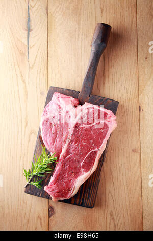 Raw t-bone or porterhouse steak with a sprig of fresh rosemary on a vintage wooden board , overhead view on wood with copyspace Stock Photo
