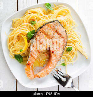 Healthy grilled salmon steak rich in omega-3 fatty acids served on linguine pasta topped with fresh basil , overhead view Stock Photo