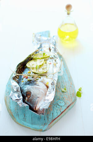 Preparing a whole fresh fish to be baked on a barbecue in a foil wrapper with lemon, olive oil , spices and herbs arranged on a Stock Photo