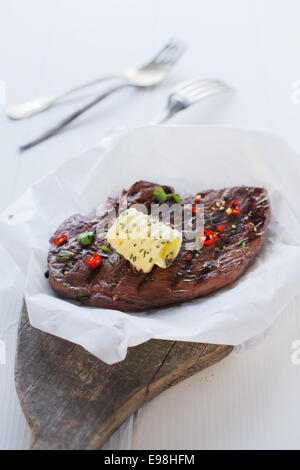 Barbecued lamb seasoned with pepper, herbs and a butter curl served on a rustic wooden board on crumpled white paper at a summer picnic Stock Photo