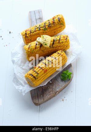 Grilled corn on the cob topped with a butter curl and served at a summer outdoor picnic on crumpled white paper on wooden board Stock Photo