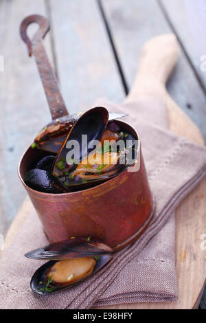 Serving of delicious gourmet freshly steamed marine mussels in a copper pot with an open one displayed below on a napkin in a rustic kitchen Stock Photo