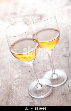 Two glasses of white sherry wine standing touching viewed high angle on a rustic wooden garden table in sunlight Stock Photo