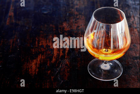Glowing cognac or brandy in an elegant snifter glass on an old dark wooden bar counter with copyspace, high angle view Stock Photo