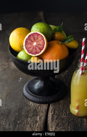 Bowl of assorted fresh citrus fruit with a halved blood orange with its distinctive red pulp in the foreground with a bottle of Stock Photo