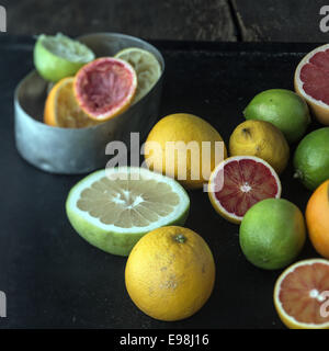 Juicing a selection of fresh citrus fruit with grapefruit, oranges, limes and lemons and a metal container with squeezed skin remnants Stock Photo