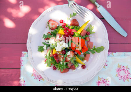 Tasty Summer Salad Melon, Strawberry, Redcurrants and Wild Flowers on Pink Wooden Background Stock Photo