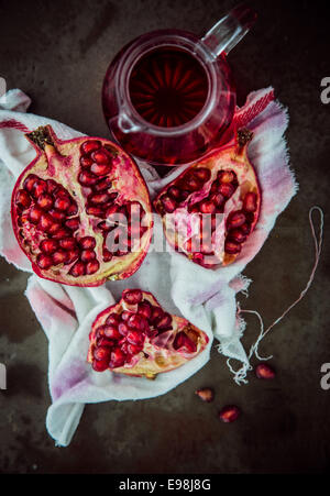 Making fresh pomegranate juice with an overhead view of a broken open fruit displaying the ripe red seeds on a stained muslin cloth with a jug of freshly prepared juice alongside Stock Photo