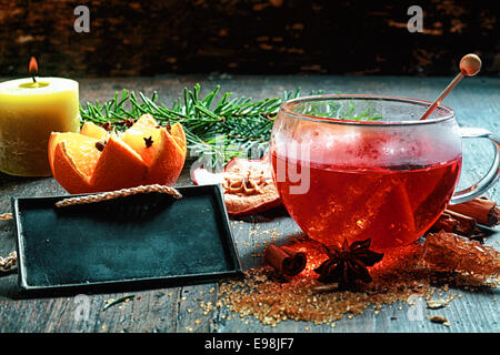 Christmas Eve spiced hot tea or gluhwein with crystallised sugar, a decorative orange and spices alongside a burning candle and Stock Photo