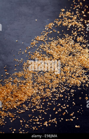 Baking or festive background of brown sugar crystals scattered on a dark surface at an oblique angle with copyspace for your Christmas greeting or message Stock Photo