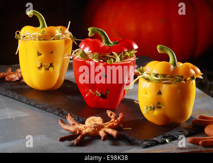 Halloween themed salad with stuffed red and yellow sweet peppers with cutout faces like jack-o-lanterns served with a flying bat pastry on a curved bark plate Stock Photo