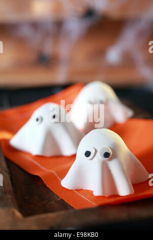 Halloween party decorations from folded pastry dough in the shape of scary little ghosts with big eyes on an orange napkin with Stock Photo