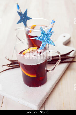Two festive glasses of Christmas mulled wine or punch seasoned with spices and orange slices served with a straw decorated with Stock Photo