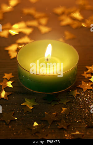 Green Christmas candle burning with glowing light surrounded by small golden decorative star shapes, high-angle close-up Stock Photo