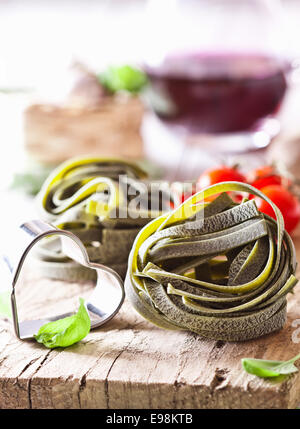 Uncooked ribbon Tagliatelle pasta and a bottle chianti wound in a ball standing on a rustic wooden surface with fresh basil and Stock Photo