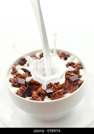 Pouring milk with a splash of droplets into a bowl of crunchy choc chip breakfast cereal rich in wheat, oats and bran for an energising low-CI start to the day Stock Photo